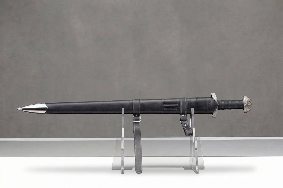 Blackfjord Viking Sword: Black leather viking sword in scabbard with silver fittings, white stitching, on clear stand, grey background