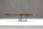 Titanforge Greatsword: sheathed greatsword in tooled brown leather scabbard with hanging strap steel guard and pommel on grey concrete background